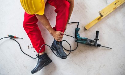 An accident of an unrecognizable male worker at the construction site. A man with an injured leg sitting on the floor. Top view.